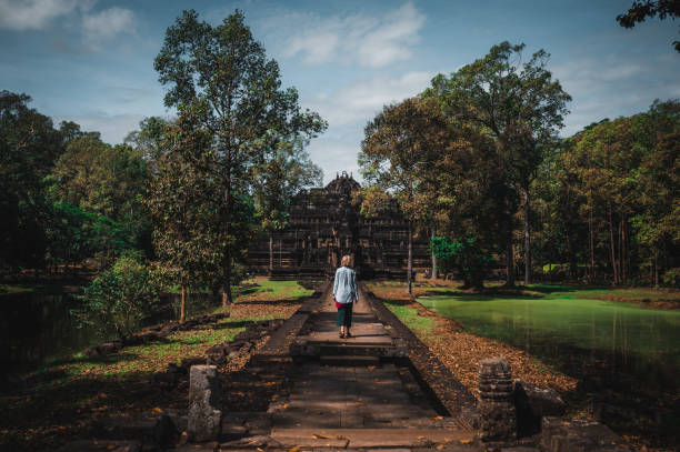 Rear view of a young blond woman walks towards the Baphuon Temple in the Angkor temple complex in Cambodia.