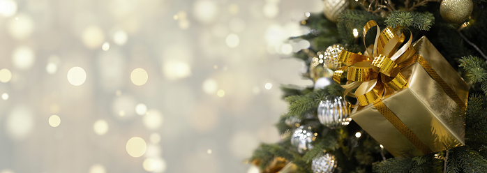 Panoramic banner background Golden Christmas defocused lights gold bokeh with decorated Christmas tree golden gift, balls, green branches. Copy space, selective focus, place for text, mockup