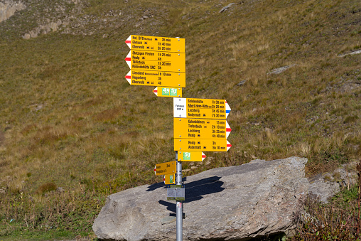 Beautiful scenic landscape with yellow hiking trail signs at summit of Swiss mountain pass Furkapass on a sunny late summer day.
