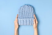 Flat lay fashionable blue knitted winter hat in female hands on blue background top view. Stylish woolen hat, concept of winter accessories for the cold. Advertising, shopping, winter sale