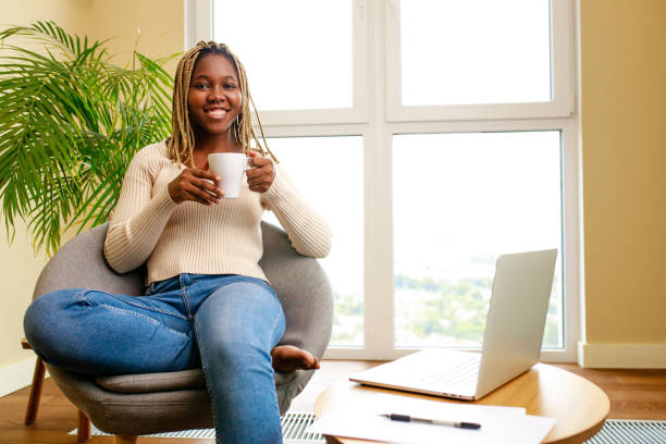 istock woman with dreadlocks reading and writing some papers sitting on couch at table with laptop 1447617896
