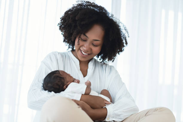 smiling african american mother holding newborn baby in her arms. loving black mom hug embrace small baby child, relax enjoy tender family moment in bedroom. beautiful family, mother's day concept. - mother baby new kissing imagens e fotografias de stock