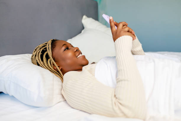 latin american woman using phone after awake in bed stock photo