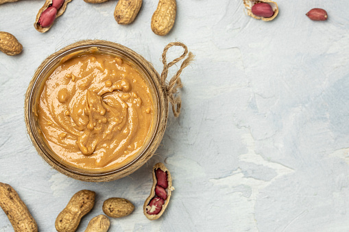 peanut paste in an open jar. creamy peanut butter peanuts scattered. top view.