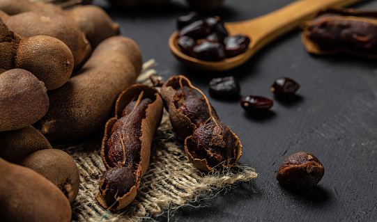 Tropical fruits, Tamarindo beans in shell on a brown butchers block on a dark background, healthy fruit. banner, menu, recipe place for text, top view.
