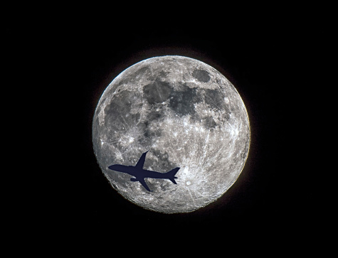 Airplane flying against full moon in night sky