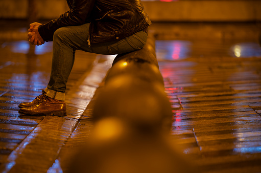Adult man sitting on street at night on a raining day. Madrid, Spain