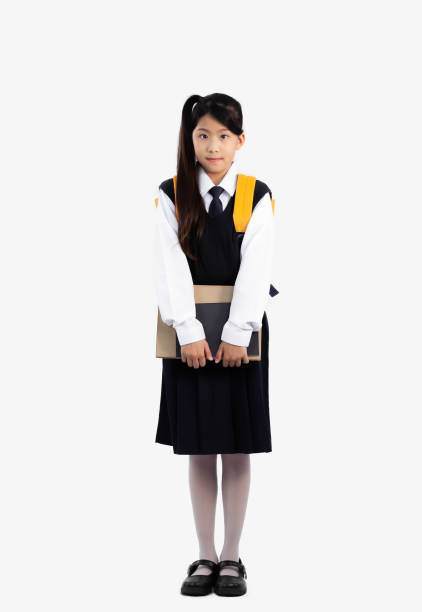istock Junior school student in british international uniform standing carrying backpack and holding books posing full length white background. 1447630067