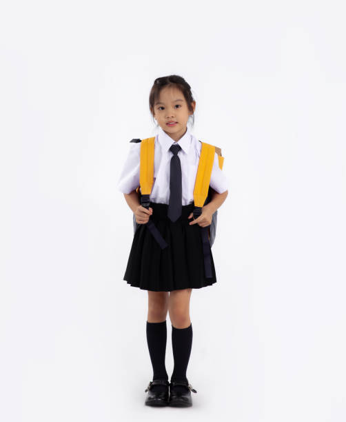 Junior school student in uniform with yellow backpack standing full length white background. Back to school.