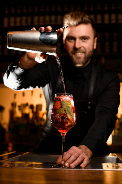 selektiver fokus auf glas mit eiswürfeln, in denen barkeeper akkurat cocktail einschenkt - pouring liquid syrup red stock-fotos und bilder