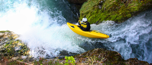 Man in yellow kayak going over a big waterfall. Extreme sports in nature. Danger on river.
