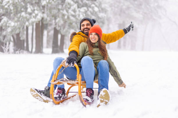 istock Couple sitting on sled and sliding down the hill while on winter vacation 1447632088