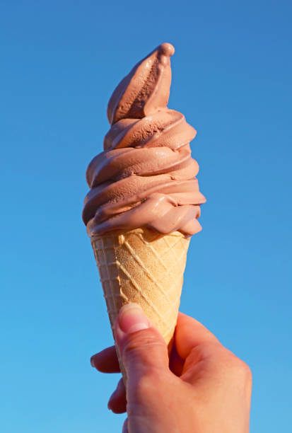 istock Mouthwatering Chocolate Soft Serve Ice Cream Cone in Hand Against Blue Sunny Sky 1447633521