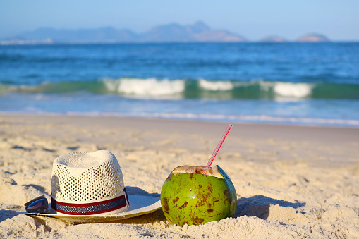Fresh young coconut with Straw hat and sunglasses on the sandy beach of Copacabana, Rio de Janeiro, Brazil, South America