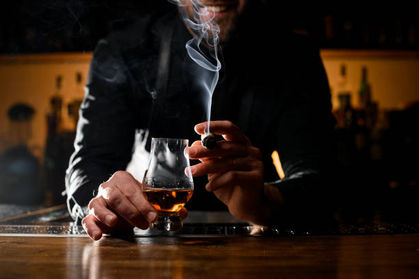 beautiful view of male hands holding a glass of alcoholic drink and smoking cigar - transparent holding glass focus on foreground imagens e fotografias de stock