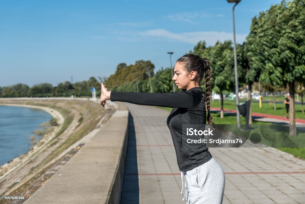 Young self loved teenage girl fitness exercises outdoor as morning routine for self-awareness of healthy life. Good posture woman stretching her muscles before workout training. Active Lifestyle Stock Photo