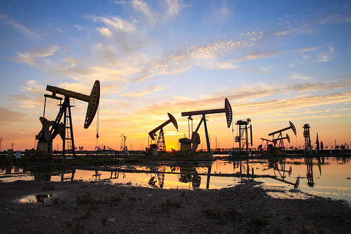 Sitio del campo petrolero, por la noche, las bombas de petróleo están funcionando, La bomba de aceite y la hermosa puesta de sol reflejada en el agua photo