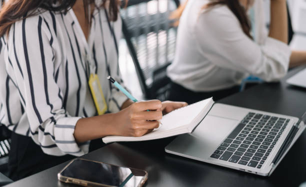 istock Closeup image of a woman writing and taking note on notebook with laptop in office. 1447641257