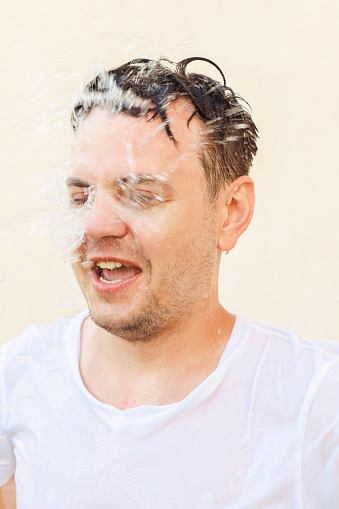 Jet of water, water splash flying in man male face. Shocked young caucasian european white man with open mouth, portrait, mental health, cold training, lifestyle.