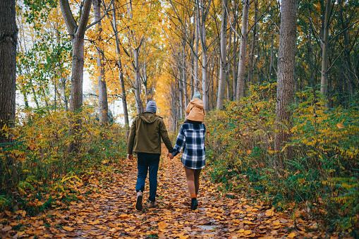 Loving couple on a walk in the forest on a cold autumn day. A woman is carrying a child on her shoulders. They are all smiling.