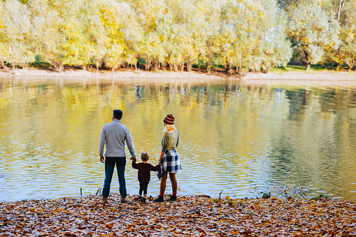 Man and woman with a child standing on the shore of the lake on a sunny autumn day and enjoying the view.
