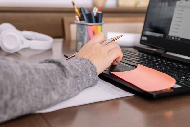 istock Close-up of a woman's hand taking notes in front of a computer 1447650692