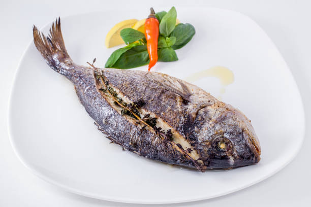 istock Baked dorado stuffed with lemons and spinach with basil, red capsicum on a white plate and light background. Horizontal orientation 1447652053