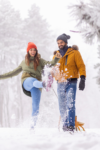 Beautiful young couple in love having fun on winter vacation, enjoying snowy foggy day in the mountain, kicking and throwing snow
