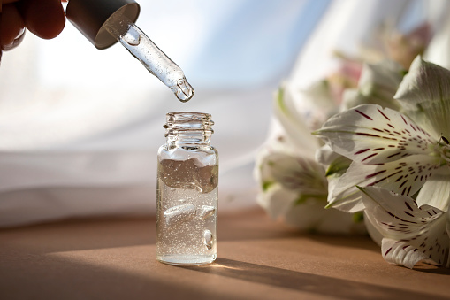 Glass dropper bottle with moisturizing lotion on the background of a bouquet of flowers. Facial skin care concept. Side view.