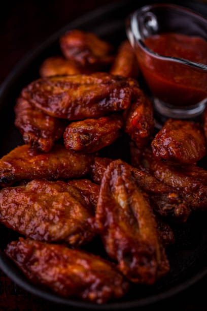 istock Deep-fried chicken wings with sauce, on a black oval platter. Vertical orientation 1447658810