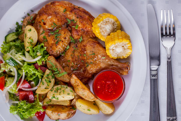 poulet frit avec sauce, maïs, pommes de terre, oignons, salade sur une assiette ronde blanche avec couverts. orientation horizontale - rotisserie chicken barbecue grill food photos et images de collection