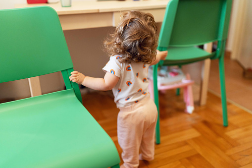 Baby girl making her first steps alone with support from furniture in the kitchen