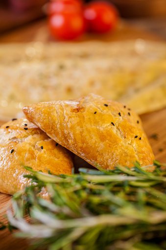 Samsa with cherry tomatoes, sesame seeds, rosemary and olive oil on a wooden board. Vertical orientation