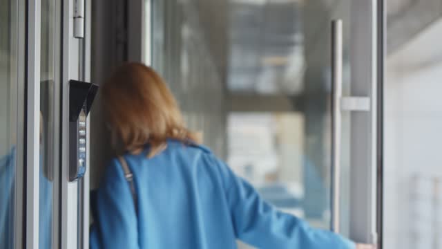 Mature woman scanning fingerprint on alarm system entering business center