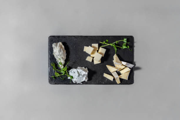 istock Cheese snacks. On a slate, black, rectangular board are pieces of goat cheese, brie cheese, philadelia cheese with dill, sour cream with herbs and microgreen pea sprouts. The board lies on a gray, paper background. 1447667578