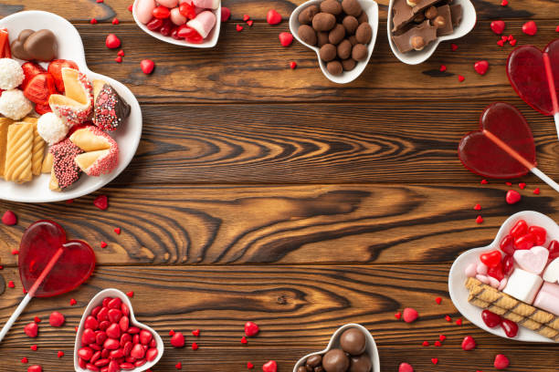 valentine's day concept. top view photo of heart shaped dishes with sweets chocolate jelly candies lollipops and cookies on wooden table background with empty space in the middle - valentines day candy chocolate candy heart shape imagens e fotografias de stock