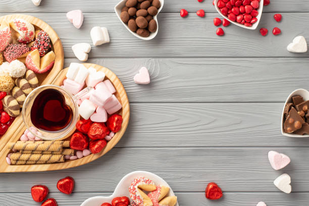 valentine's day concept. top view photo of wooden heart shaped serving tray glass of beverage saucers with sweets candies chocolate cookies on grey wooden desk background with copyspace in the middle - valentines day candy chocolate candy heart shape imagens e fotografias de stock