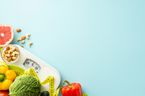 Balanced diet concept. Top view photo of scales vegetables fruits grapefruit sweet pepper almonds cashew and tape measure on isolated pastel blue background with empty space
