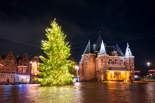 Amsterdam Christmas tree at the Waag building on the Newmarkt square with Christmas lights illuminating the pine tree in the evening.