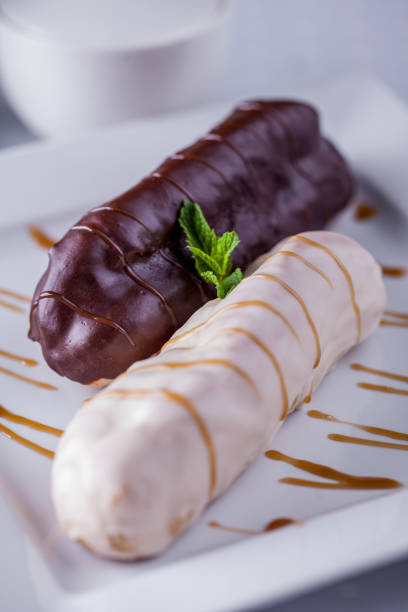 istock Dessert eclair with white and milk chocolate on top and mint on a white plate and light background. Vertical orientation 1447671866