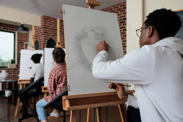 istock Young painter sitting in front of white canvas drawing vase model 1447673156