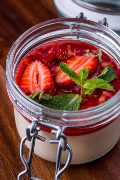 Panna cotta in a jar with strawberry jam and strawberries on a wooden table. Vertical orientation
