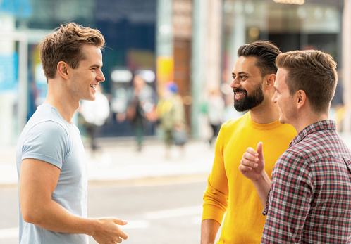 Three men in their thirties sharing a joke on the pavement of a shopping street in central London, England.