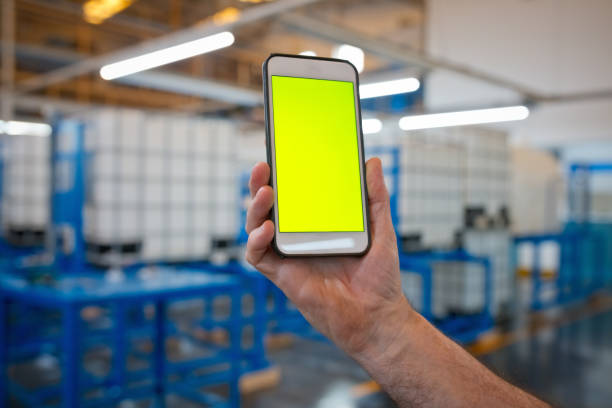 Male blue-collar worker in industry, holding smart phone. Close up of hand, unrecognizable person.