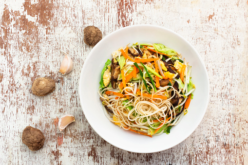 Stir fry chow mein Chinese noodles add bean sprout mushroom cabbage carrot in plate on wood background, top view, healthy vegetarian food concept.