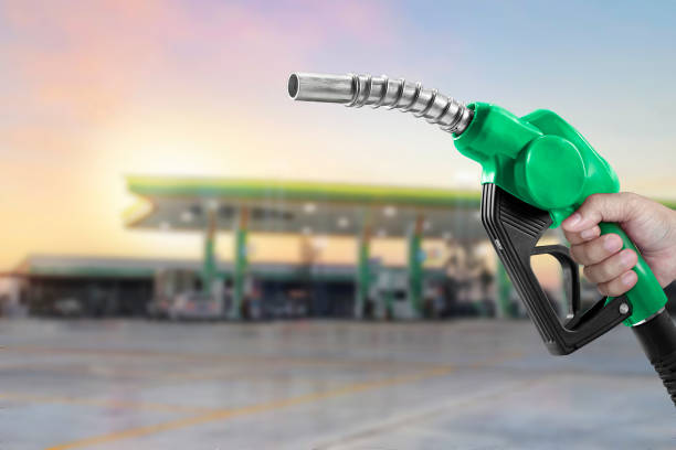 holding a fuel nozzle against with gas station blurred background - biodiesel fotos stockfoto's en -beelden