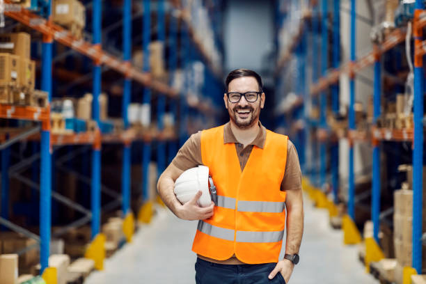 A proud supervisor posing at storage with helmet in hands and smiling at the camera. stock photo