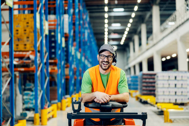 A storage worker posing on forklift and smiling at the camera. stock photo