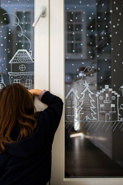 istock Child girl decorating windows for Christmas with white pencil 1447689372
