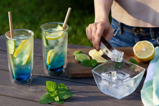 女の子は夏のさわやかなカクテルブルーラグーンを作ります。グラスにアイスキューブを追加するクローズアップ。選択的焦点 - close up women horizontal citrus fruit ストックフォトと画像